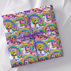 May include: A square gift package wrapped in colourful paper featuring a repeating pattern of SpongeBob SquarePants and Patrick Star riding white unicorns against a backdrop of rainbows, clouds, and flowers, tied with a thin purple ribbon.