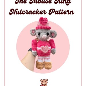 May include: A crocheted mouse toy in a pink and gray outfit, with a heart on its chest and a heart-shaped hat. The text "The Mouse King Nutcracker Pattern" is displayed above the toy, with the TalentLys logo at the top and bottom.