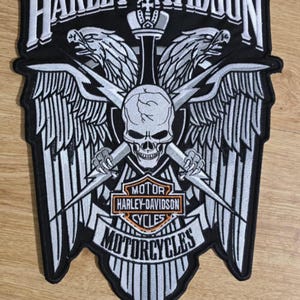 Op de afbeelding: Zwart-witte geborduurde Harley-Davidson motorfiets patch met een schedel, twee adelaars en de woorden "Motor Harley-Davidson Cycles Motorcycles".