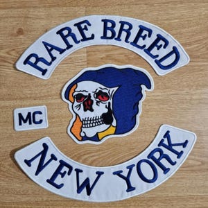 Puede incluir: Parche bordado blanco y azul con el texto "RARE BREED MC NEW YORK" y una calavera con capucha azul con acentos naranja y amarillo.