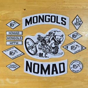 Può includere: Una collezione di toppe bianche e nere con testo e illustrazioni. Le toppe includono le parole "MONGOLS", "NOMAD", "MFFM" e "IN MEMORY OF FALLEN BROTHERS". Una toppa centrale raffigura un motociclista su una moto.