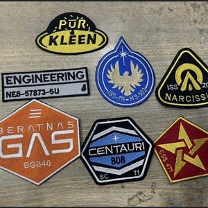 Może przedstawiać: Zbiór siedmiu haftowanych naszywek z różnymi wzorami i tekstami. Naszywki są w różnych kolorach, w tym niebieskim, czerwonym, pomarańczowym, żółtym i czarnym. Tekst na naszywkach zawiera "PUR KLEEN", "ENGINEERING NE8-57873-5U", "BERATNAS GAS BG840", "ISS-416-MS-502", "ISS 204 NARCISSUS", "CENTAURI 808 SC 11" i "CSS 471".