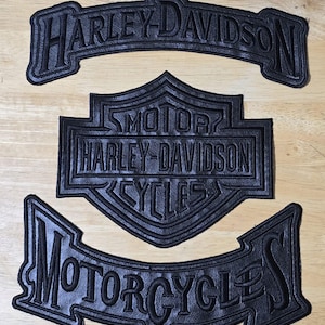 Può includere: Tre toppe in pelle nera Harley-Davidson. La toppa superiore recita "Harley-Davidson". La toppa centrale è il logo Harley-Davidson con "Motor?" sopra e "Cycles" sotto. La toppa inferiore recita "Motorcycles".