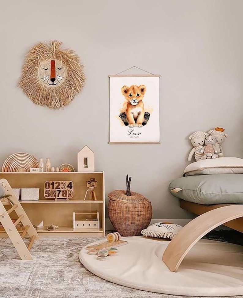 May include: A nursery room with a light brown wooden shelf with a toy camera, wooden blocks, and a wooden toy house. There is a light brown wicker basket, a light brown wooden rocker, and a white rug with a light brown rug underneath. A framed print of a lion cub with the name Leon is hanging on the wall. A light brown woven lion head is hanging on the wall.