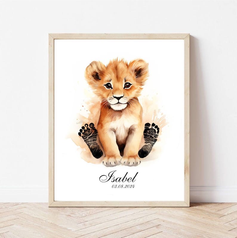 May include: A watercolor painting of a lion cub with black paw prints. The painting is framed in a light wood frame and includes the name "Isabel" and the date "03.08.2021".