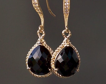 May include: Gold dangle earrings with black teardrop-shaped stones and a rope-like design. The stones are faceted and have a high shine.