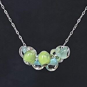 May include: A silver chain necklace with a cluster of green and blue glass beads. The beads are round and have a translucent appearance.