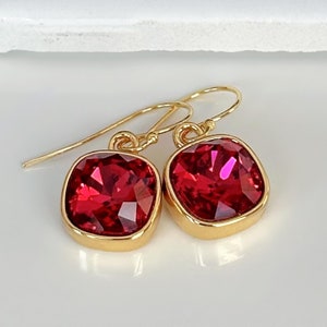 May include: Gold dangle earrings with square red crystal stones.