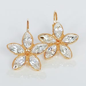 May include: A pair of gold-toned flower-shaped earrings. Each earring features five clear, marquise-cut crystals set in a floral design. The earrings have a lever-back closure.