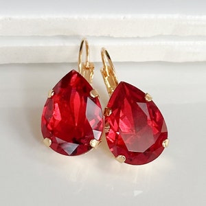 Peut inclure: Une paire de boucles d'oreilles pendantes dorées avec des cristaux rouges en forme de goutte.