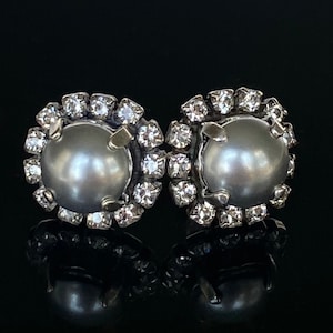 May include: A pair of silver earrings with a gray pearl center and a halo of clear rhinestones.