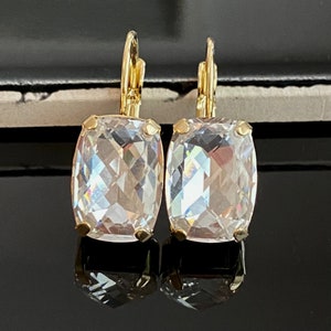 Może przedstawiać: Para złotych kolczyków z przezroczystymi, fasetowanymi, kwadratowymi kryształami.