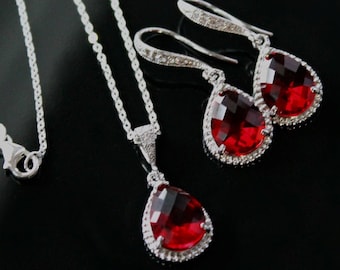 May include: A silver necklace and earrings set with teardrop-shaped red gemstone pendants surrounded by clear cubic zirconia stones.