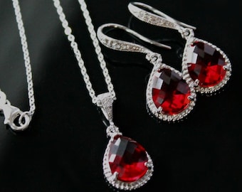 May include: A silver necklace and earrings set with teardrop-shaped red gemstones surrounded by a halo of smaller clear stones.