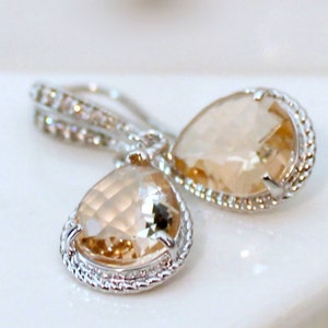 May include: A pair of silver teardrop earrings with clear, faceted, champagne-colored stones. The stones are set in a silver bezel with a decorative, rope-like border.