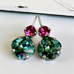 Può includere: Un paio di orecchini pendenti con un design in cristallo verde e rosa. Gli orecchini hanno una finitura argentata.