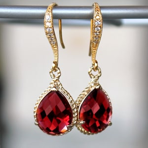 Puede incluir: Pendientes de gota de oro con una piedra roja y detalles de cristal transparente.