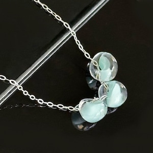 Puede incluir: Un collar de cadena de plata con tres cuentas de vidrio azul claro. Las cuentas son redondas y tienen una forma ligeramente irregular.