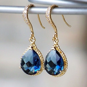 May include: A pair of gold teardrop earrings with blue gemstone accents. The earrings have a twisted rope design and are accented with small clear stones.