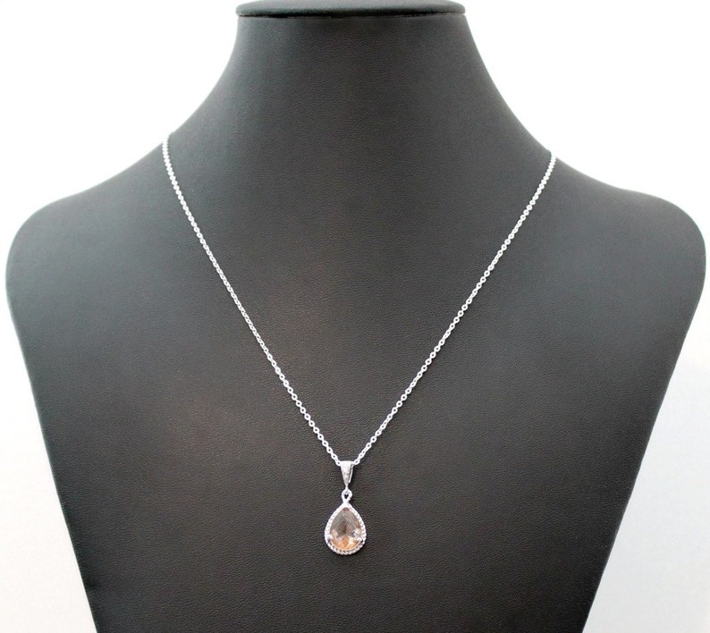 May include: A silver chain necklace with a teardrop-shaped pendant featuring a clear, light brown gemstone.