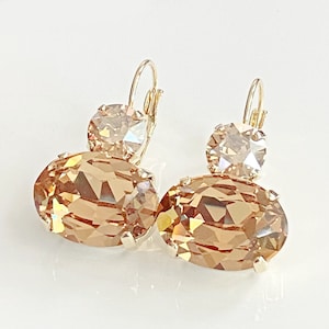 May include: A pair of gold-toned leverback earrings. Each earring features a large, oval-shaped, faceted, light brown crystal below a smaller, round, light brown crystal. The earrings are set against a white background.