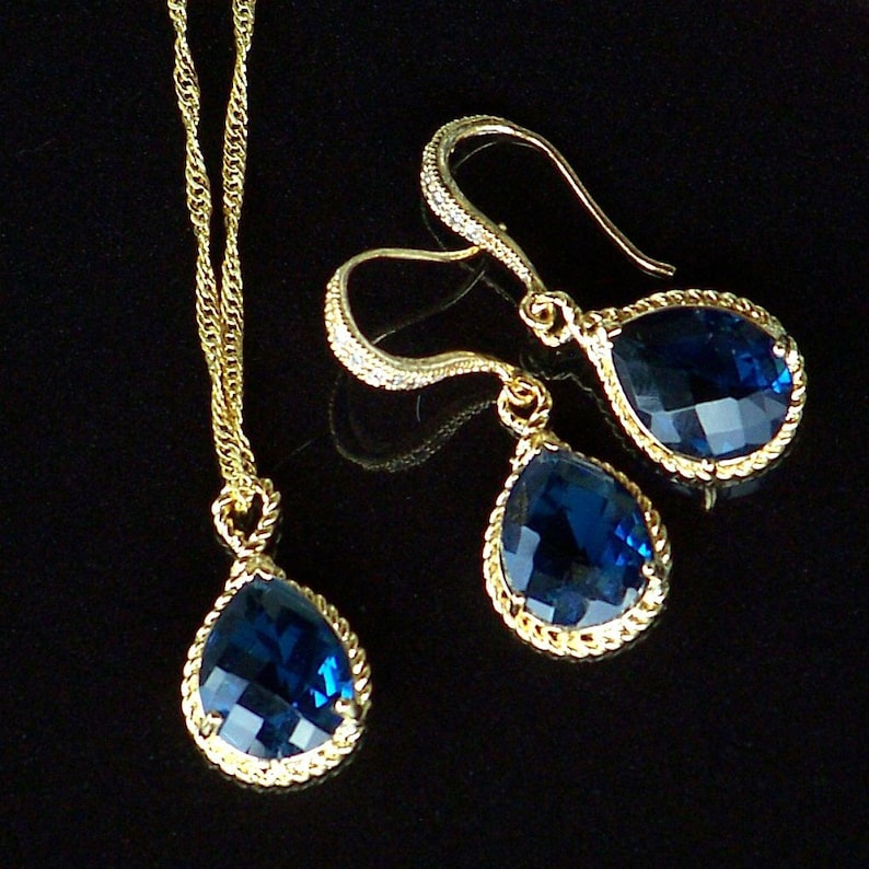 May include: A gold necklace and earrings set with teardrop-shaped blue gemstone pendants. The pendants have a rope-like gold trim.