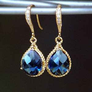 May include: A pair of gold teardrop earrings with a blue gemstone and a row of clear rhinestones on the ear wire.