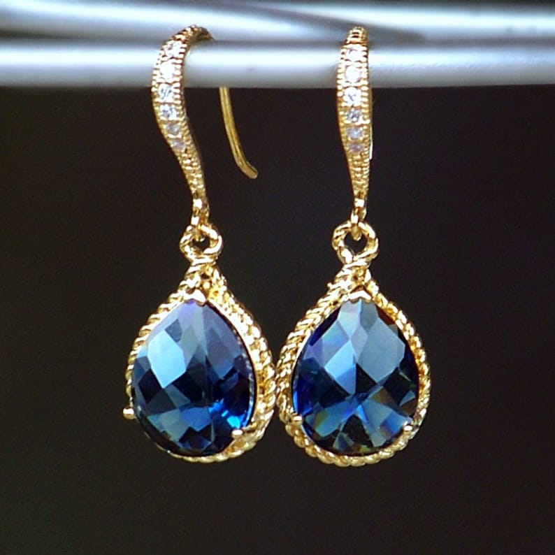 May include: A pair of gold teardrop earrings with a blue gemstone and a row of clear rhinestones on the ear wire.