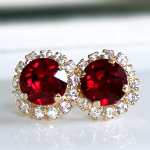 May include: A pair of gold stud earrings with a large red rhinestone surrounded by smaller clear rhinestones.