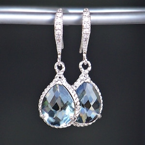 Può includere: Un paio di orecchini a goccia d'argento con pietre di cristallo trasparenti. Gli orecchini hanno un delicato design a corda attorno alle pietre.