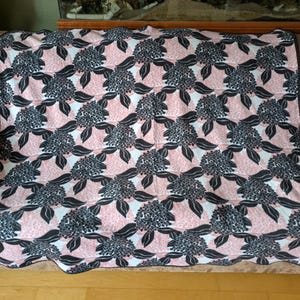 May include: A pink and black floral patterned throw blanket with a black border. The blanket is folded and placed on a brown couch.