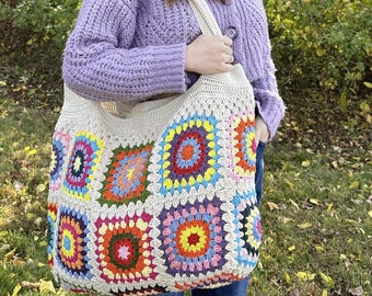 May include: A large, off-white crochet tote bag constructed from multiple colorful granny squares. The bag features a variety of vibrant hues including red, orange, yellow, green, blue, and purple, arranged in a repeating pattern with a thick strap.