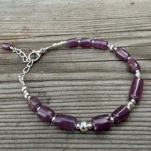 Peut inclure: Un bracelet composé de perles cylindriques violettes alternant avec de petites perles rondes argentées réfléchissantes. Le bijou comprend un fermoir mousqueton argenté et une chaînette d'extension réglable à une extrémité.