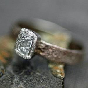 May include: A silver ring with a textured band and a square-shaped clear gemstone set in a silver bezel.