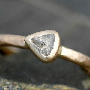 May include: A gold ring with a triangular diamond set in a bezel setting. The ring band is textured and has a hammered finish.