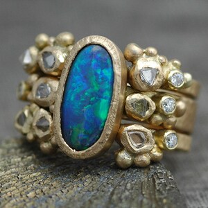 K&ouml;nnte beinhalten: Ein goldener Ring mit einem gro&szlig;en ovalen Opal-Edelstein, umgeben von kleineren Diamanten. Der Ring besteht aus mehreren B&auml;ndern mit strukturierten Golddetails.