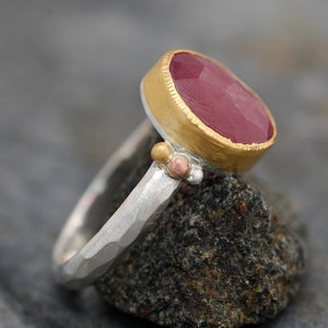 May include: A silver ring with a hammered texture and a pink gemstone set in a gold bezel. The ring is accented with small gold and copper beads.