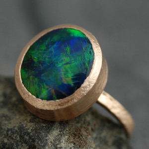 May include: A gold ring featuring a round, green and blue opal gemstone.