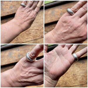 May include: A silver ring with a textured surface. The ring is worn on a person's finger.