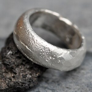 May include: A silver ring with a textured, hammered finish. The ring is wide and has a rounded shape.