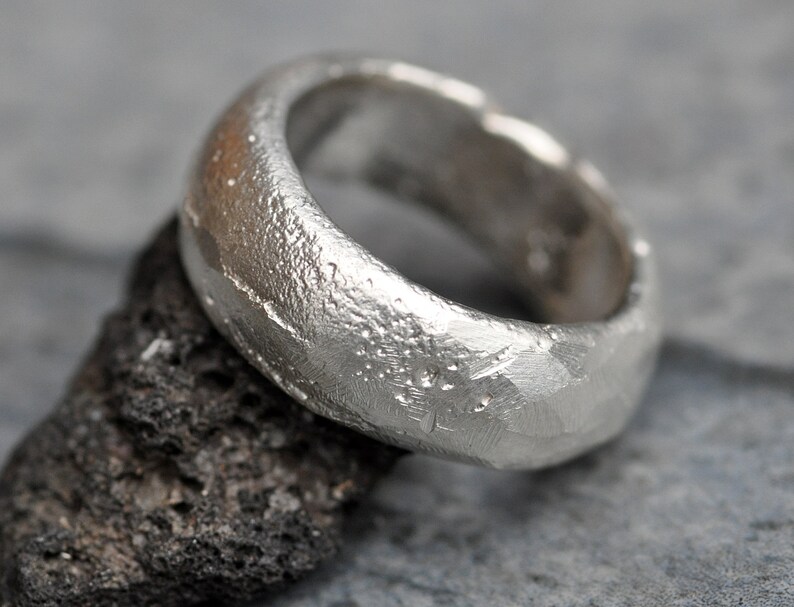 May include: A silver ring with a textured, hammered finish. The ring is wide and has a rounded shape.