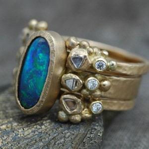 K&ouml;nnte beinhalten: Ein goldener Ring mit einem gro&szlig;en ovalen Opal-Edelstein, umgeben von kleineren Diamanten und goldenen Perlen.
