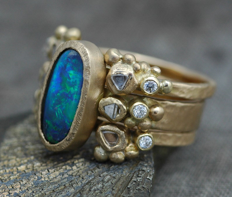 K&ouml;nnte beinhalten: Ein goldener Ring mit einem gro&szlig;en ovalen Opal-Edelstein, umgeben von kleineren Diamanten und goldenen Perlen.