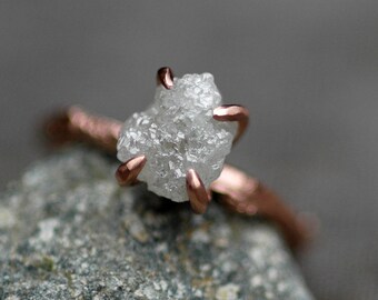 May include: A ring featuring a rough, white diamond set in a rose gold setting.
