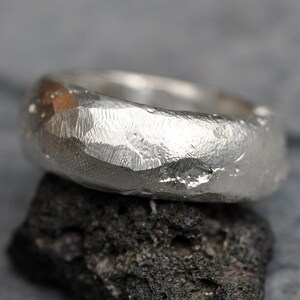 May include: A silver ring with a hammered, textured finish. The ring is thick and has a rounded shape.