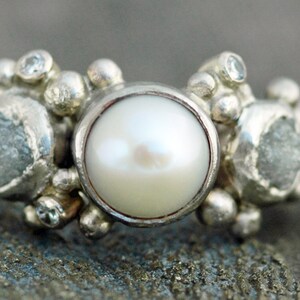 May include: A silver ring with a large white pearl in the center, surrounded by smaller white stones and silver beads.
