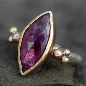 May include: A ring with a large, faceted, purple gemstone set in a gold bezel. The band is silver with small gold accents.