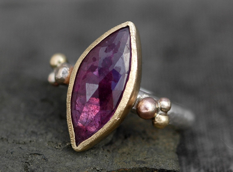 May include: A ring with a large, faceted, purple gemstone set in a gold bezel. The band is silver with small gold accents.