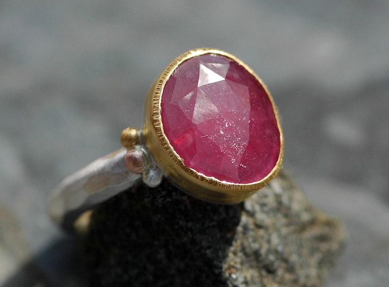 May include: A ring with a large, faceted, pink ruby gemstone set in a gold bezel. The ring band is made of hammered silver.