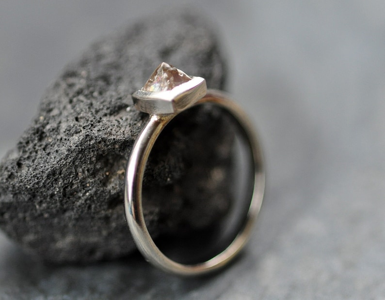 May include: A silver ring with a clear, faceted gemstone set in a triangular bezel.